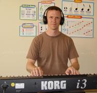 Man playing a Korg i3 keyboard wearing headphones.