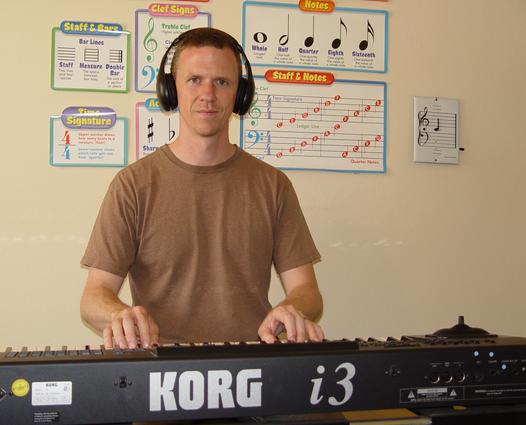 Man playing a Korg i3 keyboard with headphones in a room with music charts.