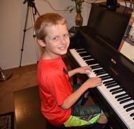 Young boy playing a piano, smiling at the camera.