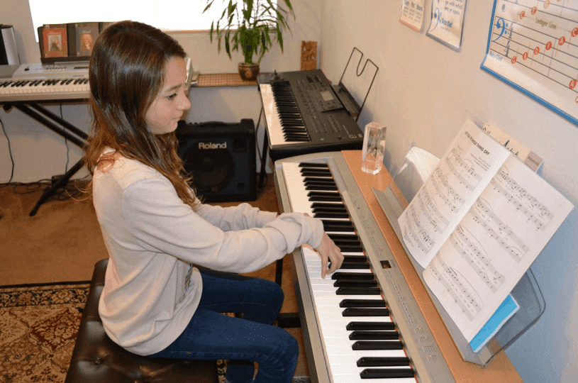 A young girl playing piano with sheet music in front.
