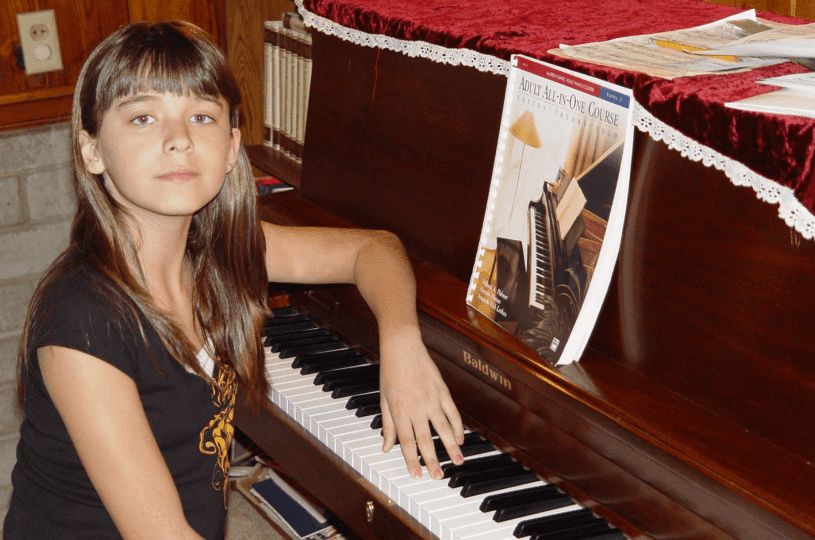 Young girl playing piano with sheet music on stand.