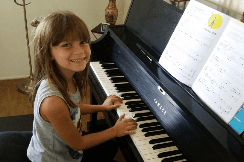 Young girl smiling while playing the piano with sheet music.