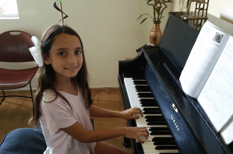 Young girl playing piano with a smile.