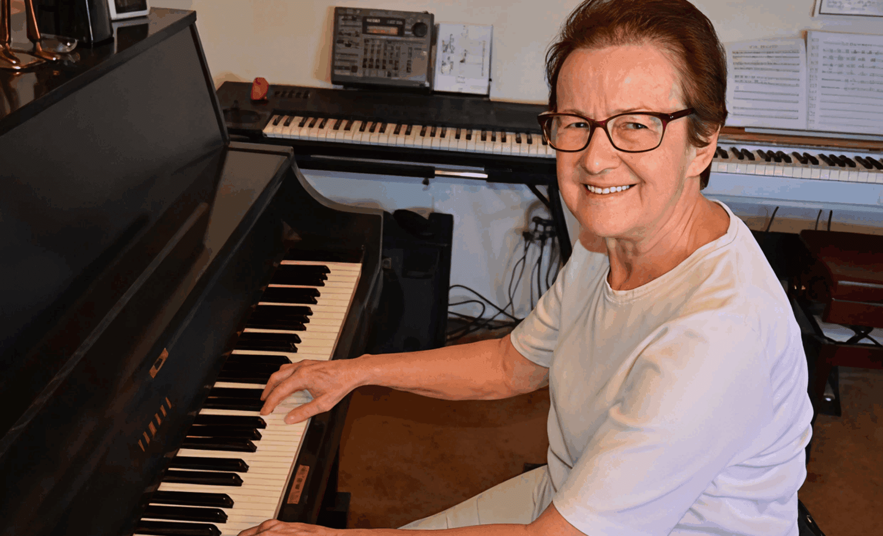Elderly woman smiling while playing piano.