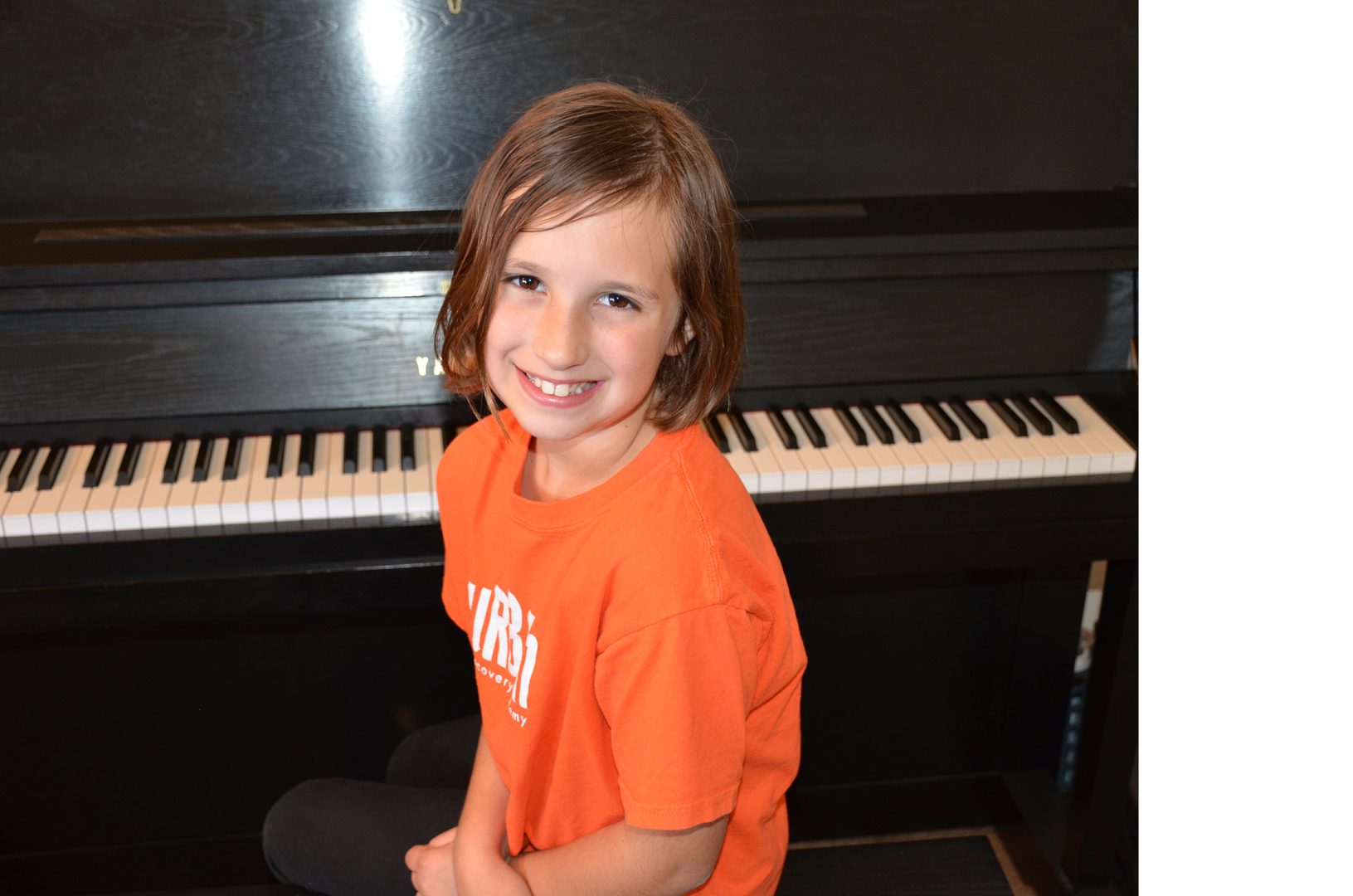 Young girl smiling in front of a piano keyboard.