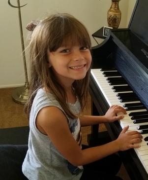 Young girl smiling while playing piano keys.