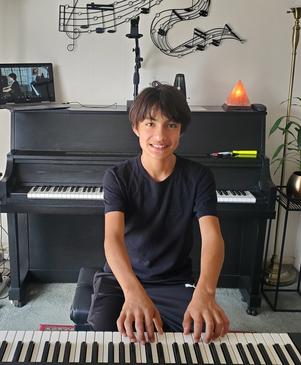 Young boy sitting in front of a piano, smiling.