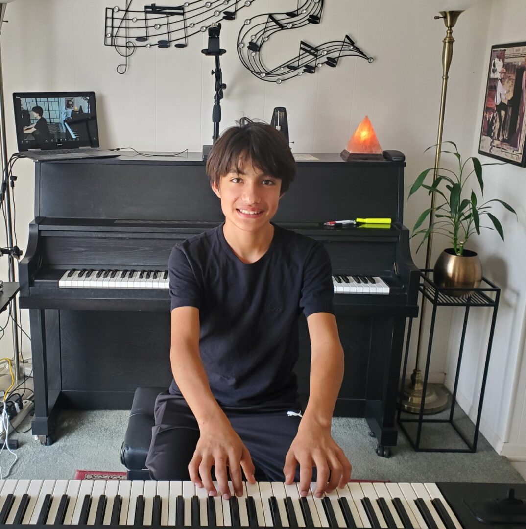 A boy playing a keyboard in a cozy room with a piano behind him.