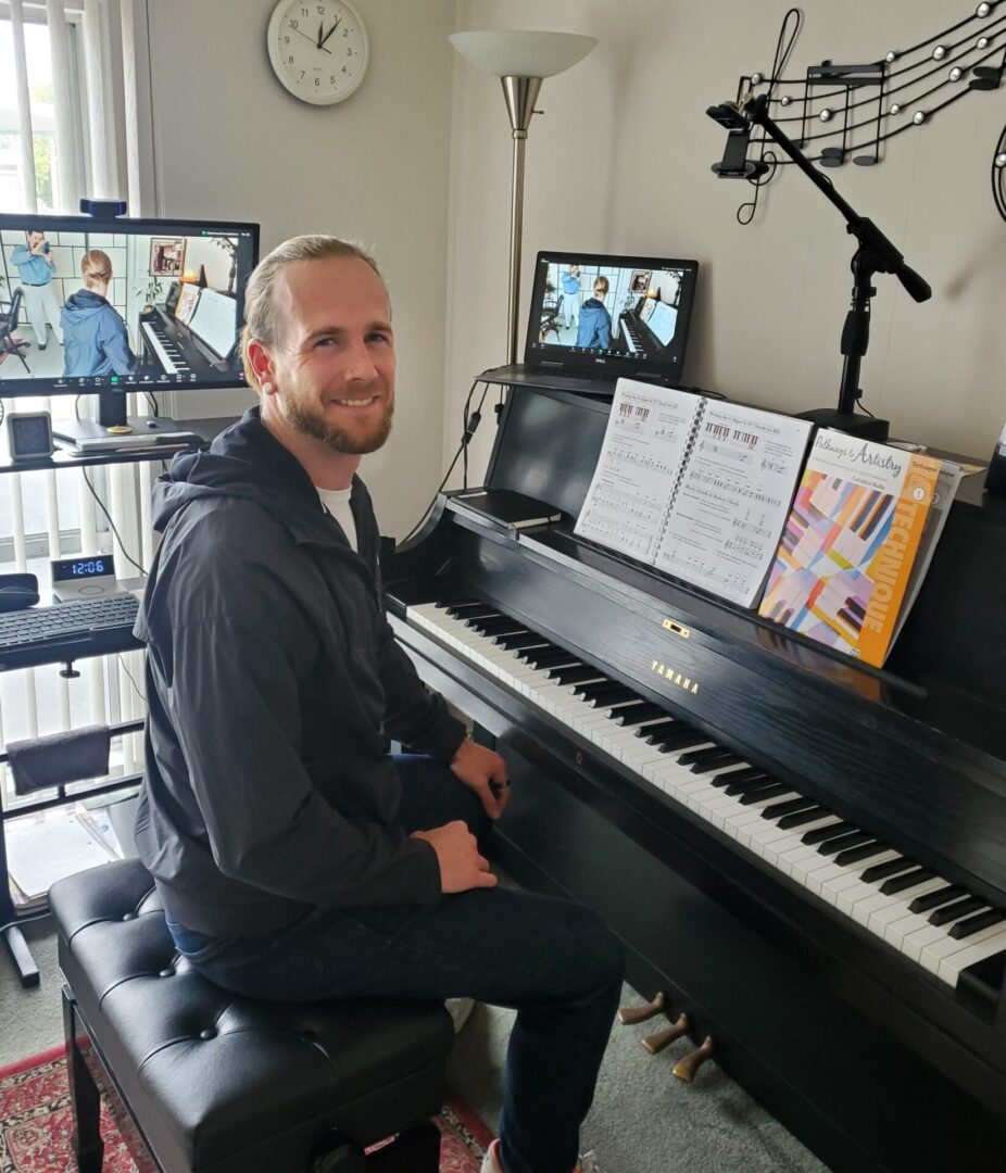 Man smiling while seated at a piano with sheet music and video call setup.