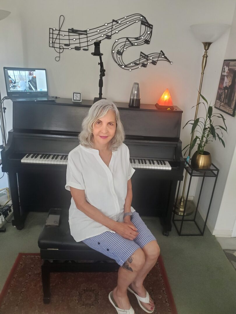 A woman sitting in front of a black piano in a cozy room.