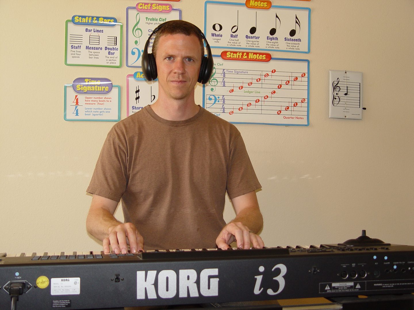 A man wearing headphones playing a Korg i3 keyboard.