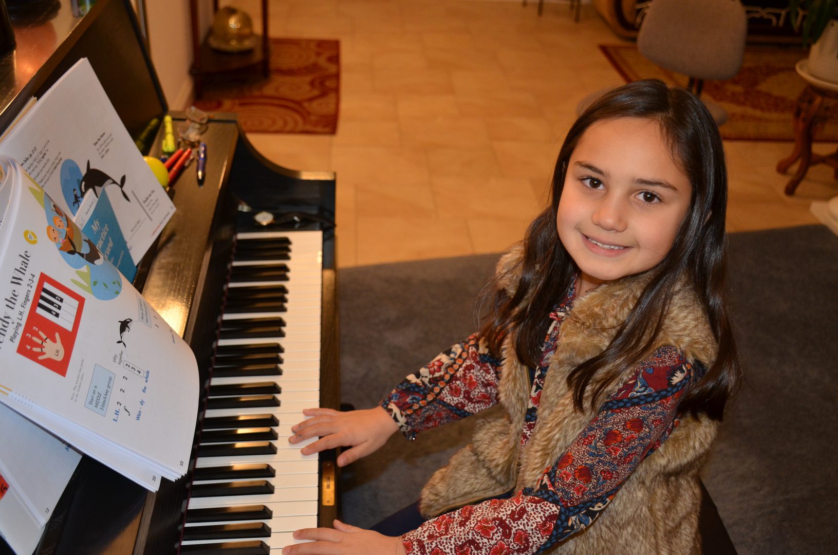 Young girl smiling while sitting at a piano keyboard indoors.