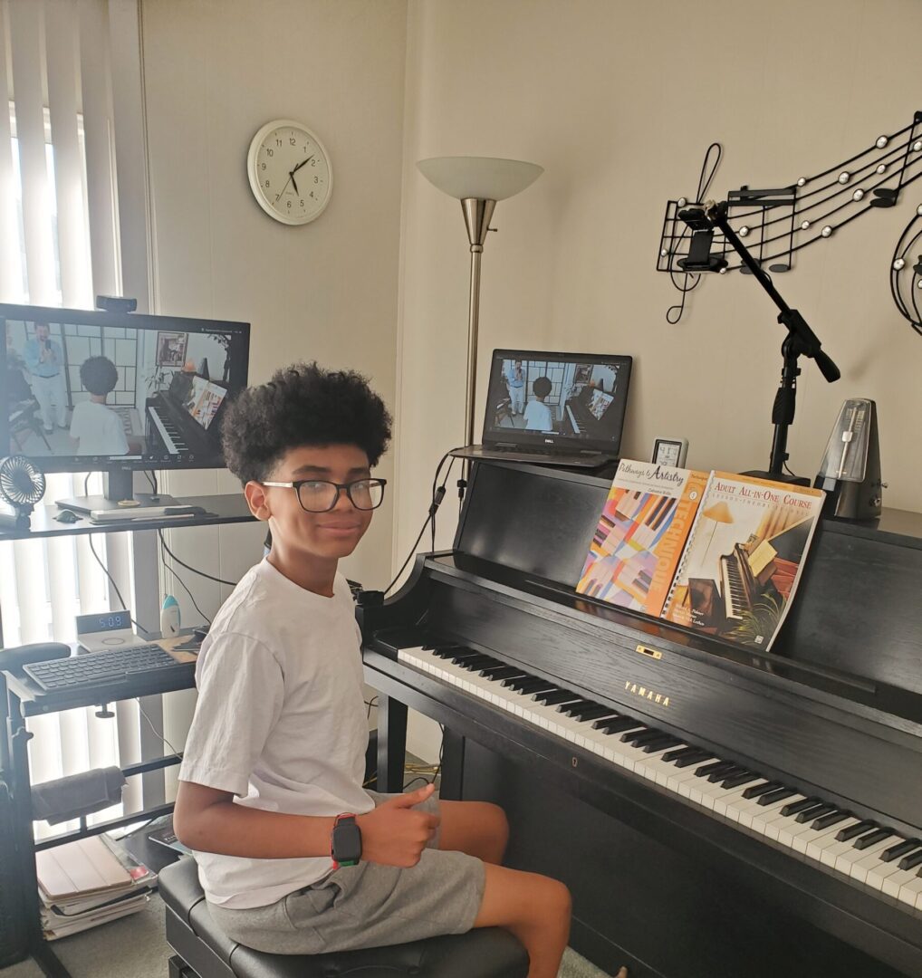 A young boy playing the piano in a well-lit room with multiple screens.