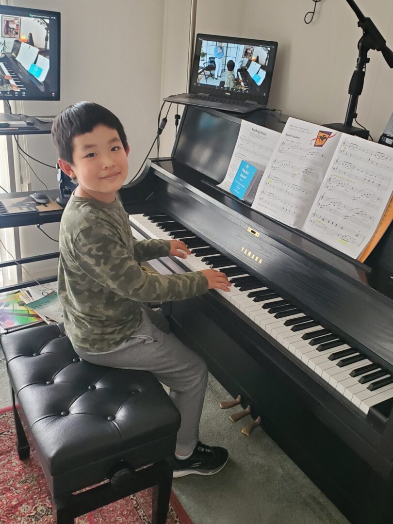 A young boy happily playing a black piano indoors.