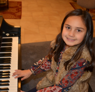 A young girl smiling while playing the piano.